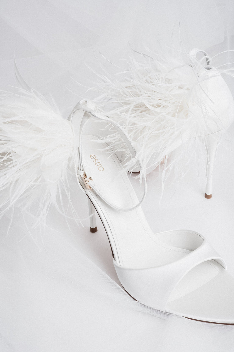Detail view of buckle and feather trim on white high heel sandals