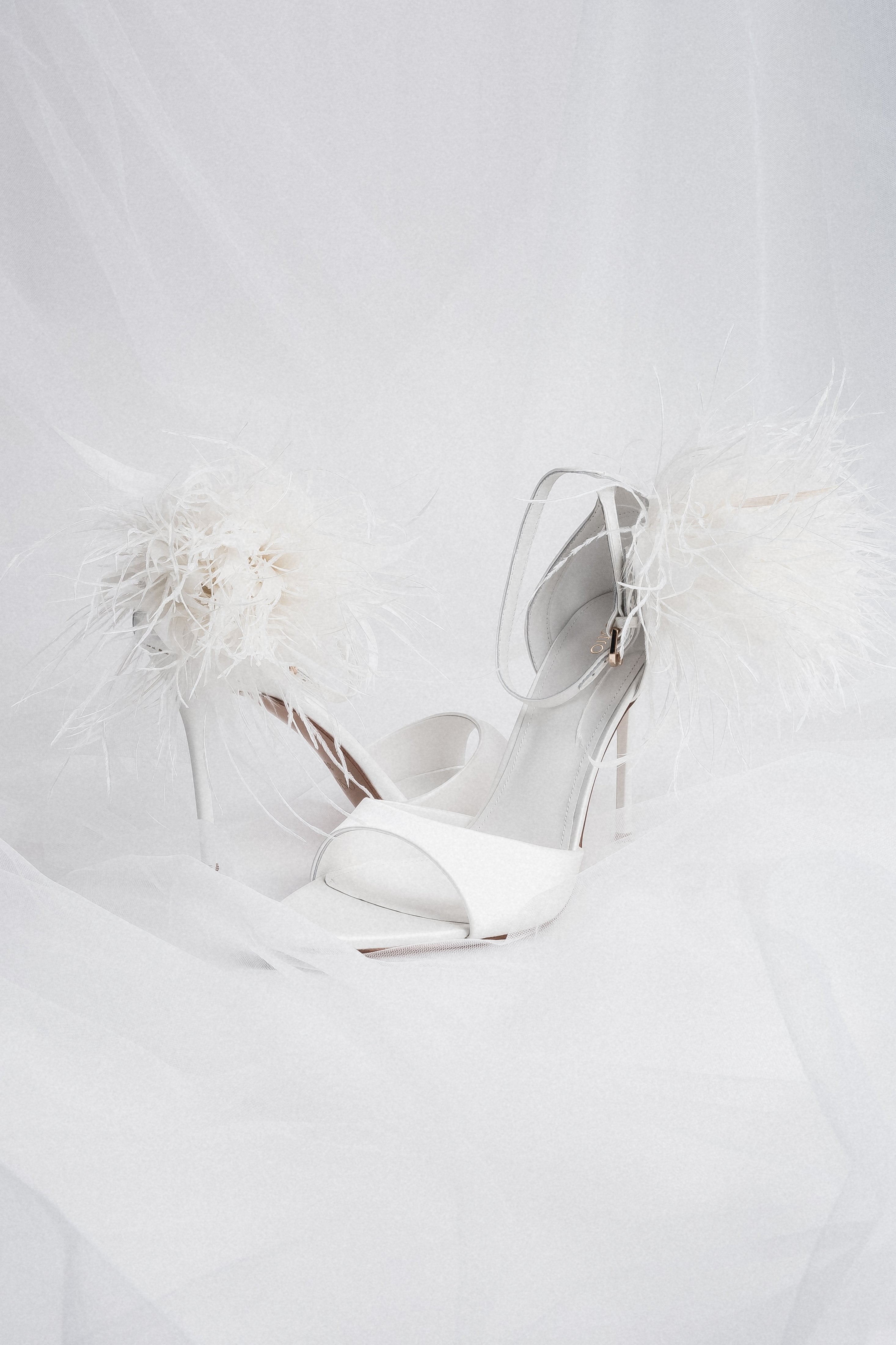 Angled view of women's white high heel sandals with feather trim