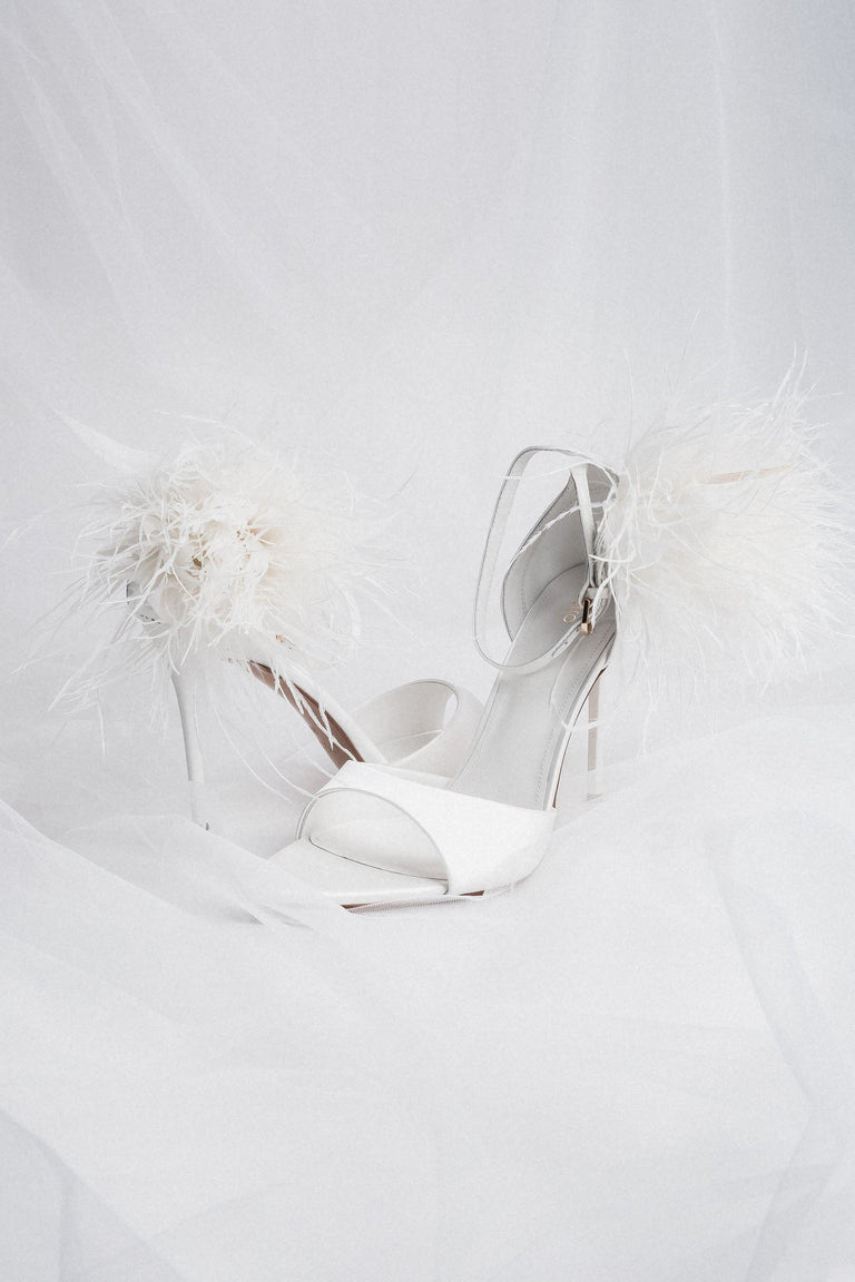 Angled view of women's white high heel sandals with feather trim