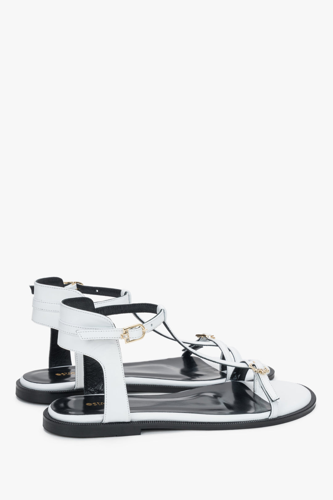 Angled view of women's white flat sandals with gold-toned buckles