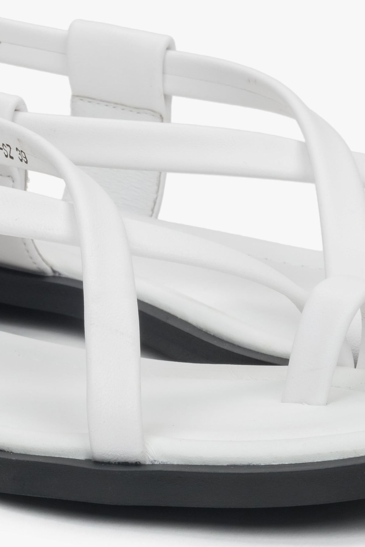 Close-up of white women’s leather sandals with a toe loop, highlighting silver details.