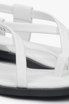 Close-up of white women’s leather sandals with a toe loop, highlighting silver details.