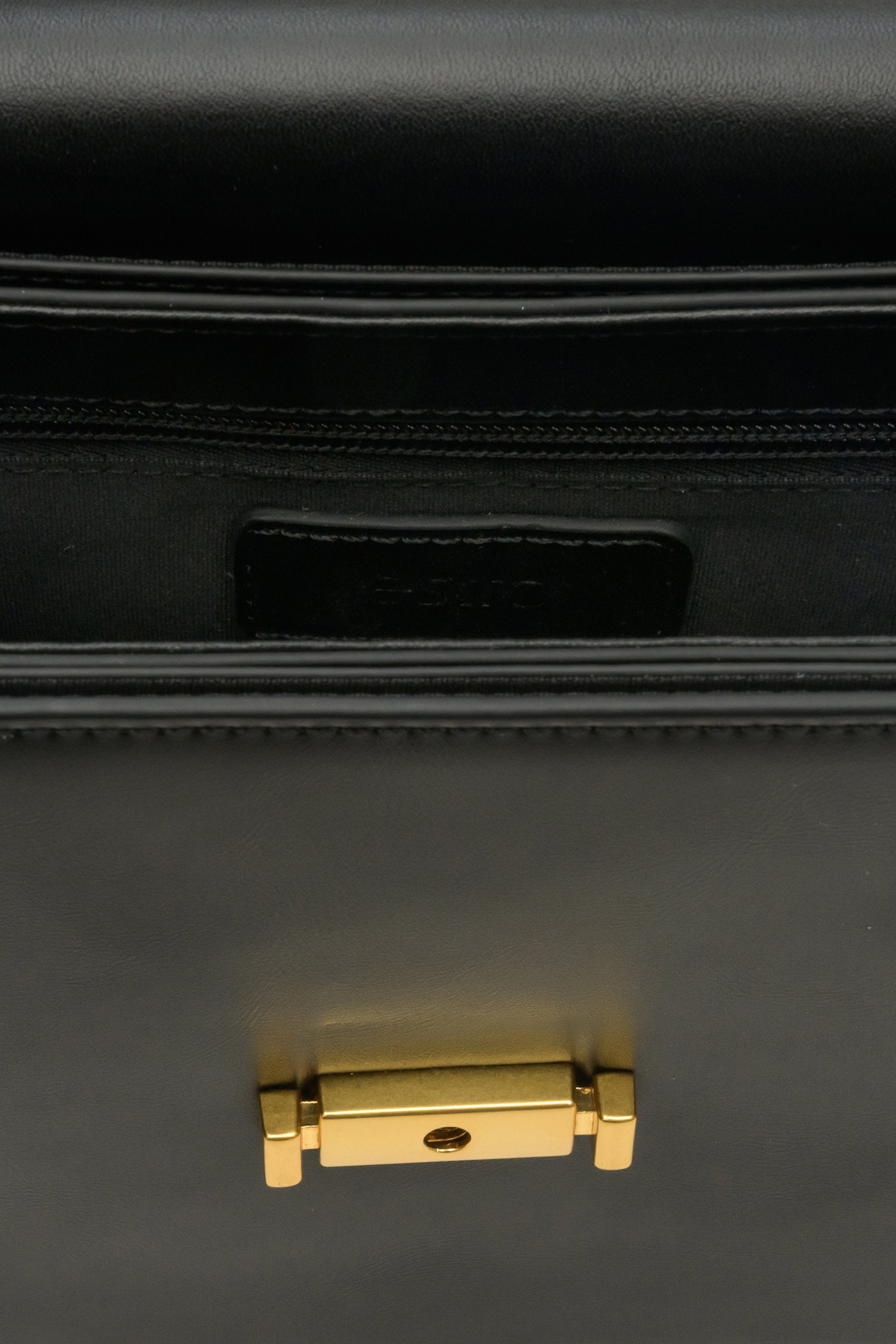 Small women's handbag made of genuine black leather with gold accents - close-up on details.