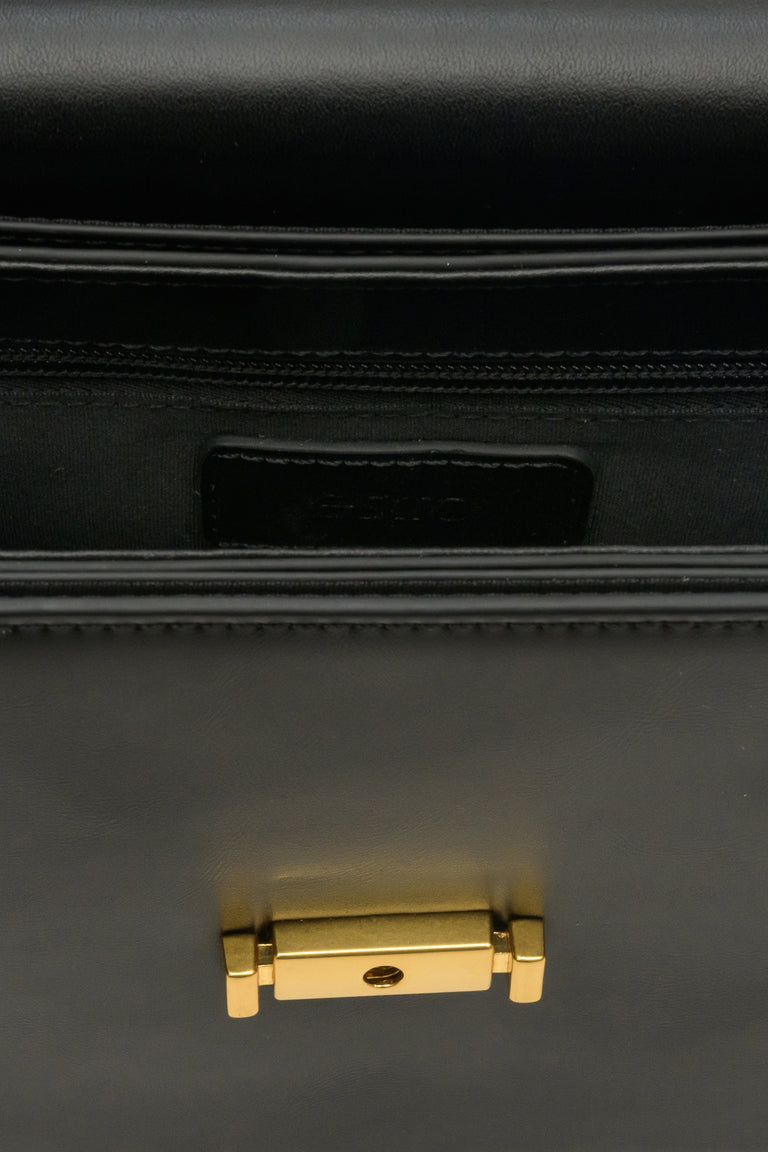 Small women's handbag made of genuine black leather with gold accents - close-up on details.