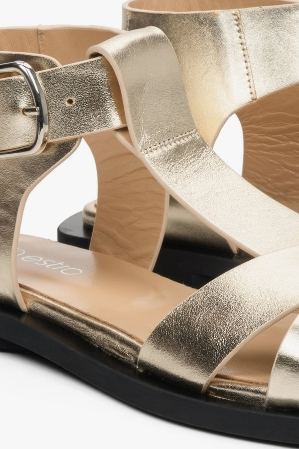 Women's leather gold sandals on a flat sole with wide straps - closeup of detail.