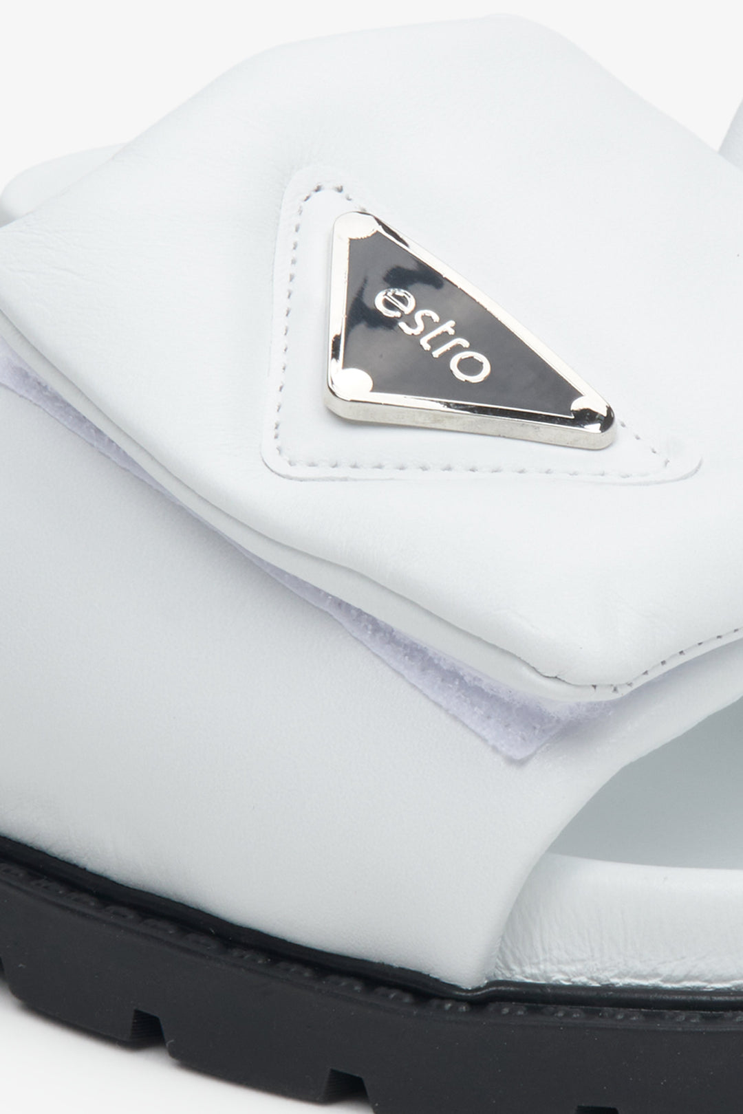 Women's white slides with a silver brand's emblem on the side on an elastic sole - close-up on the detalis.